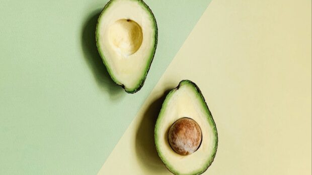 Fresh avocado halves with pit on pastel green and yellow background
