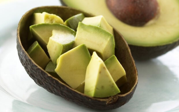Fresh avocado cubes inside the avocado shell on a white surface