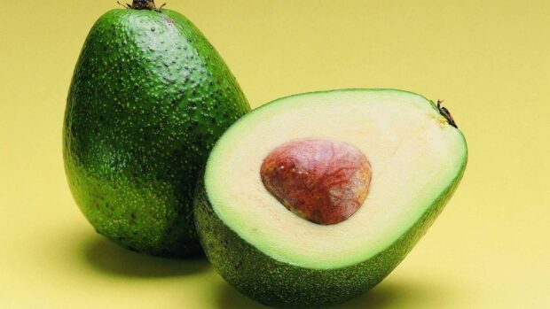 Fresh avocado cut in half showing the seed and green flesh on a yellow background