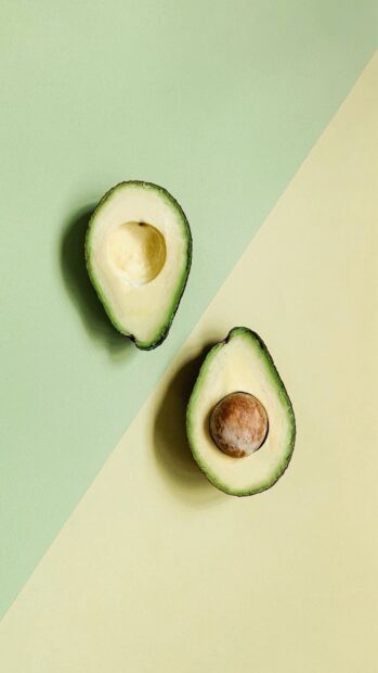 Fresh avocado halves with seed and without seed on green and beige surface