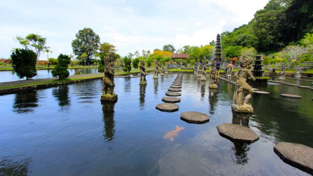 Balinese garden with stone statues and stepping stones over water in Bali