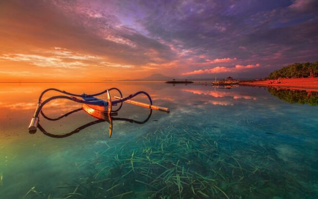 Traditional Bali boat floating on clear water during sunset in Bali