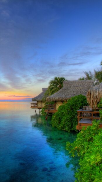 Overwater bungalows surrounded by lush greenery on Bali coast at sunset