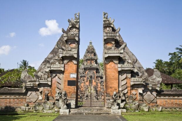 Traditional Balinese gate entrance of ancient temple in Bali surrounded by statues and greenery