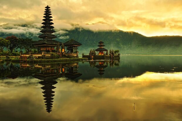 Traditional Balinese temple reflected in calm lake with mountains in the background