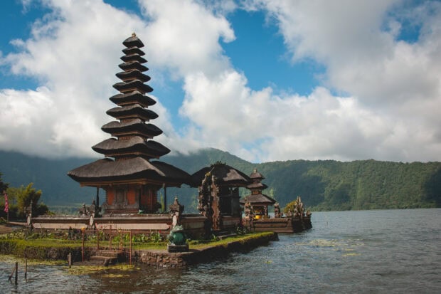 Balinese temple with traditional architecture near the lake and lush green hills in Bali