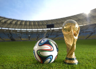 Official soccer ball Brazuca on a football field next to the FIFA World Cup trophy