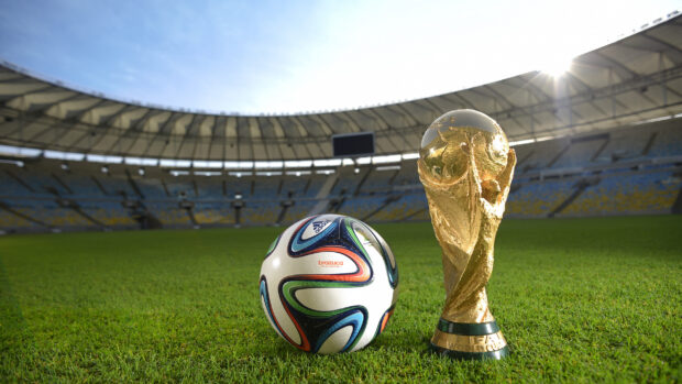 Official soccer ball Brazuca on a football field next to the FIFA World Cup trophy