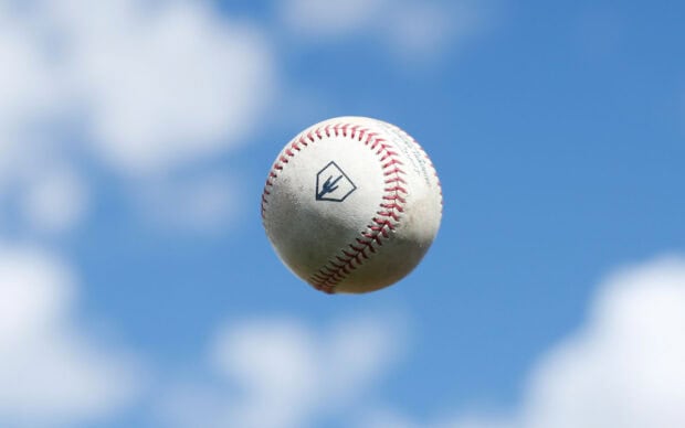 A baseball flying in the sky on a clear blue day with visible stitching and logos