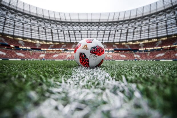 A soccer ball placed on the grass field inside a large stadium with empty seats visible in the background