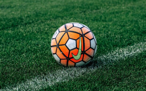 A soccer ball with orange and white panels resting on green grass near the white line