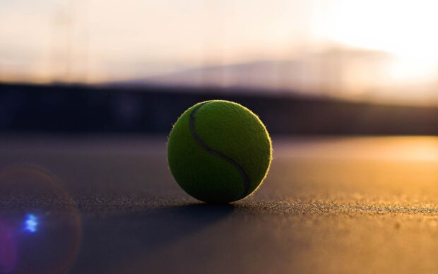 A tennis ball resting on the court with the sunset in the background