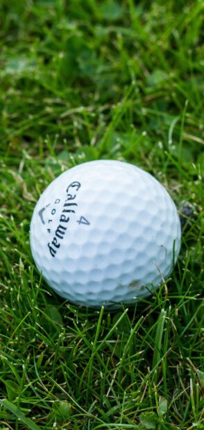 A close up of a golf ball lying on green grass on a golf course