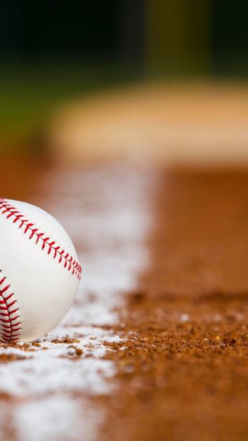 A baseball resting on the edge of the dirt field line on a baseball field