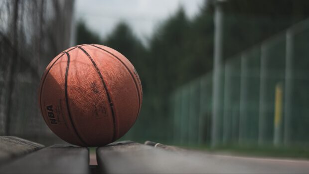 A basketball resting on a wooden bench with an outdoor court in the background