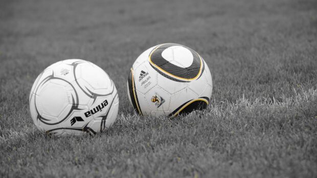 Two soccer balls lying on grass field with Adidas and Prima logos visible