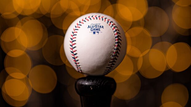 A detailed view of a baseball with red and blue stitching on a black stand with warm bokeh lights background