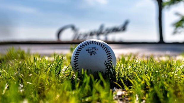 A baseball resting on green grass on a sunny day at a Cleveland field