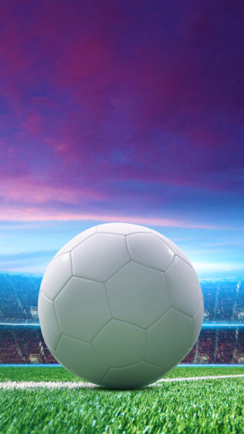 A close up of a ball on the grass field under a colorful sky at the stadium