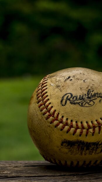 A close up of a worn baseball with red stitching on a wooden surface