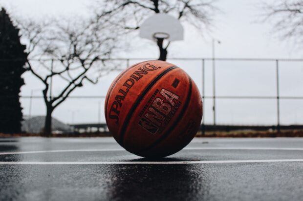 A basketball ball placed on an outdoor court with a hoop and trees in the background