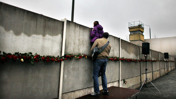 A person helping another climb over the Berlin Wall in a public commemoration event