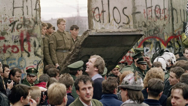 Crowd of people gathered around a piece of Berlin Wall during its fall in historical moment
