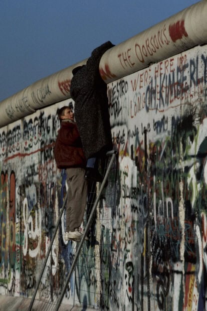 Man helping woman climb over the Berlin Wall covered in graffiti during historic event