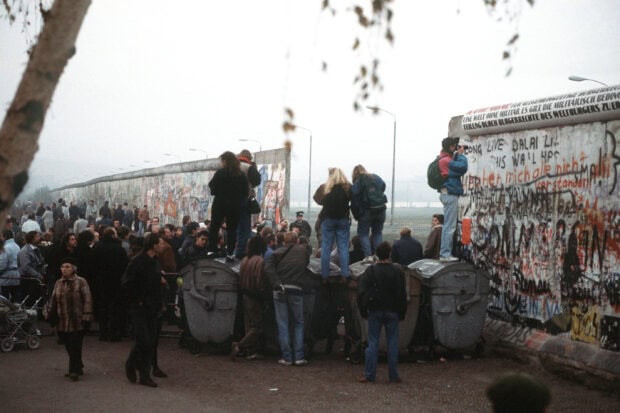 A large crowd gathering at the Berlin Wall showing vibrant graffiti and people observing the scene