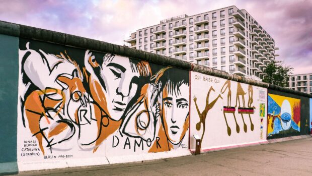 Street art on the Berlin Wall featuring expressive human faces and abstract figures in vibrant colors