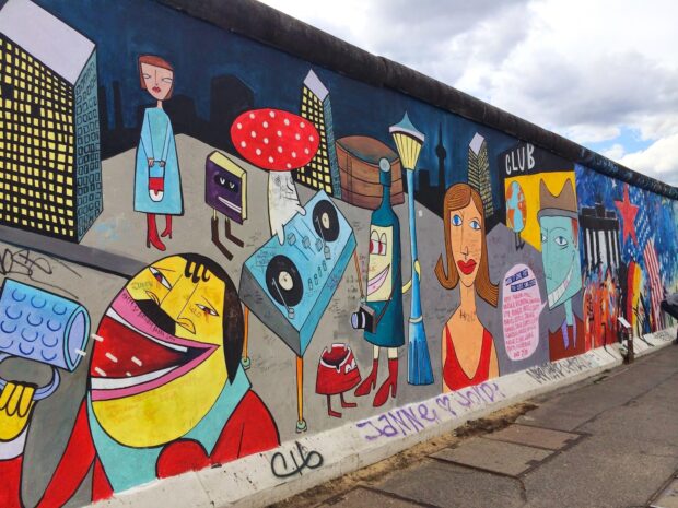 Colorful Berlin Wall graffiti featuring abstract characters and cityscape in high quality