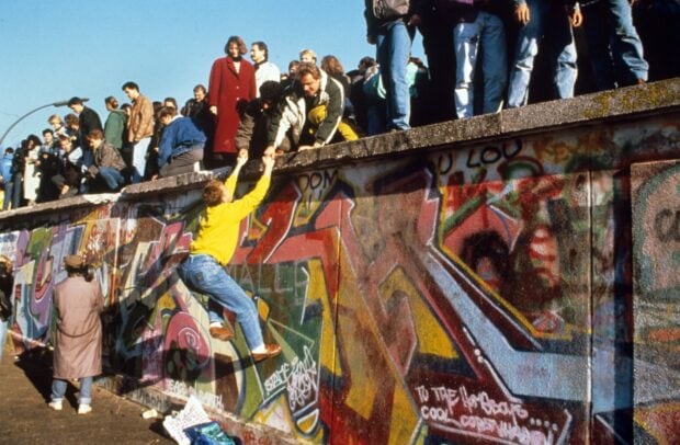 People climbing and gathering on the Berlin Wall covered with colorful graffiti during historic moments of the Berlin Wall