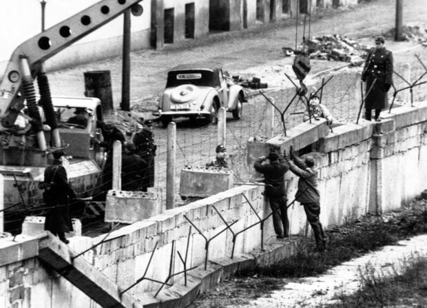 Two men attempting to cross the Berlin Wall under watchful eyes of guards