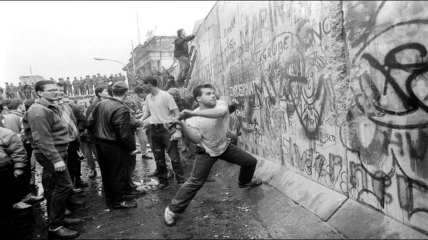 Young man throwing a rock at the Berlin Wall with a crowd watching on the street