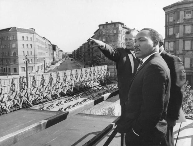 A historical moment showing civil rights leaders near the Berlin Wall in black and white photograph