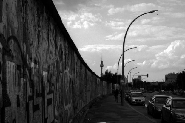 A person walking along the Berlin Wall with street lamps and cars in the background