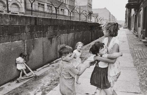 Children playing near the Berlin Wall with a scooter and holding hands in the street