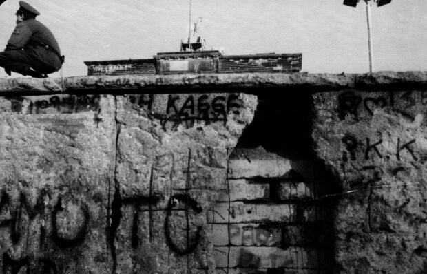 Graffiti on a section of the Berlin Wall with a guard sitting on top