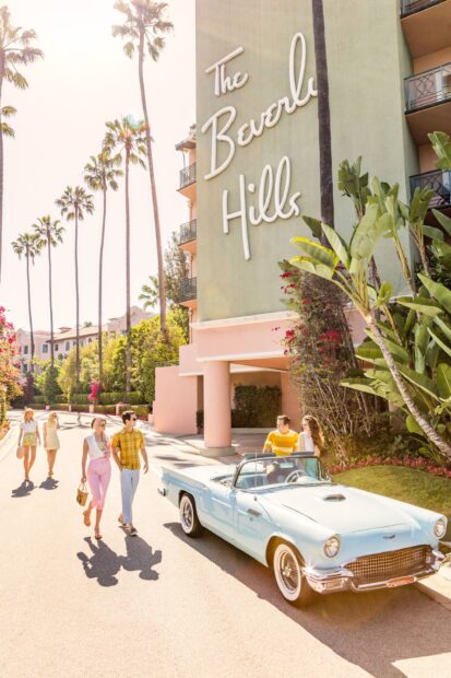 A vintage car parked outside The Beverly Hills hotel with people walking along the sunny street