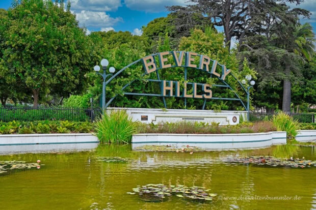 Entrance sign of Beverly Hills surrounded by greenery and water pond