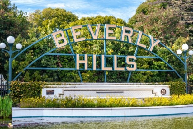 Green Beverly Hills sign surrounded by trees and flowers in HD quality