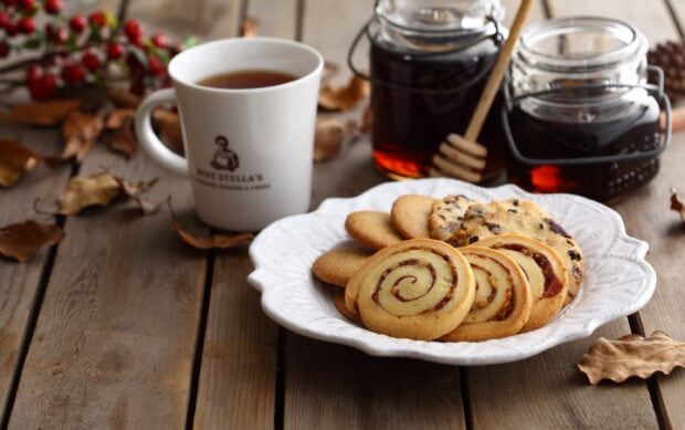 A plate of biscuit variety served with coffee and jars of honey on wooden table