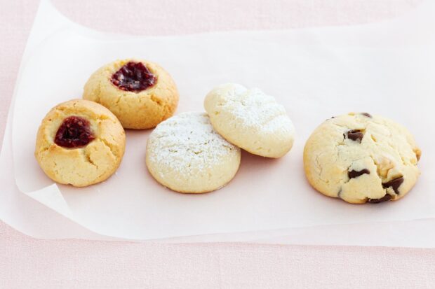 Assorted biscuit with jam, powdered sugar and chocolate chips on parchment paper