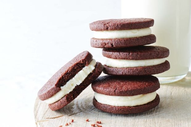 Cream filled biscuit stack on a wooden surface with a glass of milk in the background