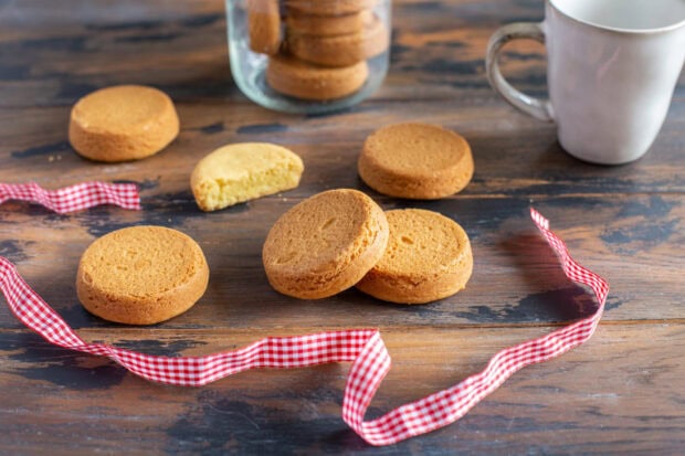 Golden biscuit pieces laid on a wooden table with a red checkered ribbon and a white mug nearby