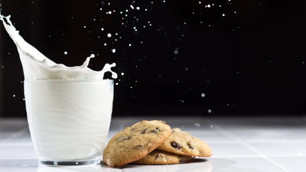 Chocolate chip biscuit next to glass of milk with splash on black background