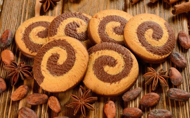Swirled biscuit with cocoa beans and star anise arranged on wooden surface