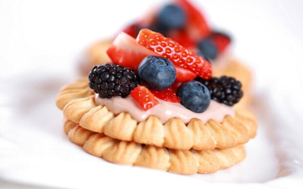 A close up of biscuit topped with cream and fresh berries including strawberries blueberries and blackberries