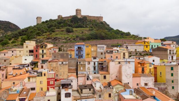 Colorful buildings of Bosa Italy with medieval castle on hill in the background