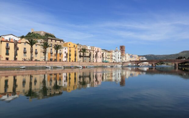 Colorful buildings in Bosa Italy reflecting on the river with a clear blue sky and bridge